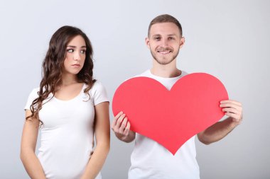 Gri arka plan üzerinde kırmızı kağıt kalp tutan güzel genç çift