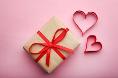 Pembe arka planda kırmızı kalpleri olan hediye kutusu.