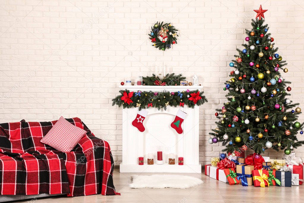 White decorated fireplace near sofa and christmas tree on brick wall background