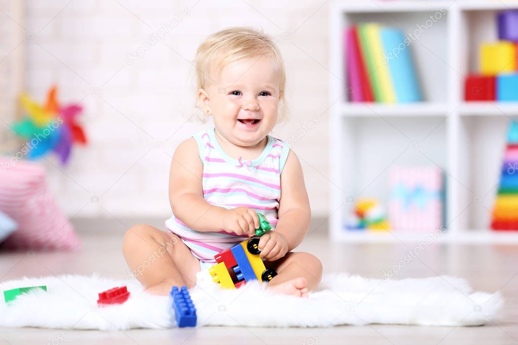 Baby girl sitting on white carpet with toys