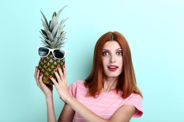 Ananas güneş gözlüğü ile nane arka planda tutan genç redhaired kadın