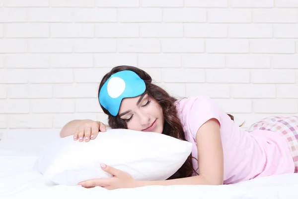 Beautiful girl with pillow and sleeping mask lying on white bed