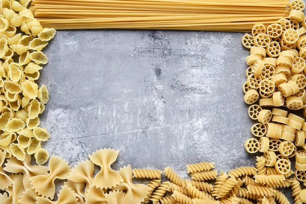 Different uncooked pasta on grey wooden table