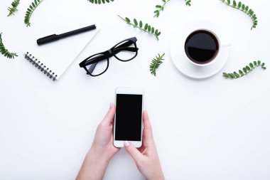 Kadın elinde fincan kahve, defter ve beyaz zemin üzerine gözlük ile Smartphone