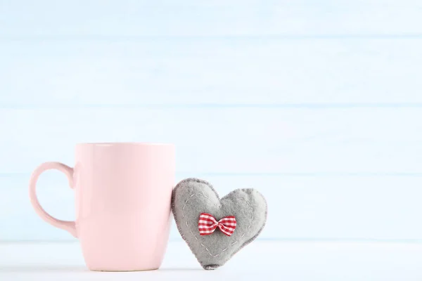 Fabric heart with cup on wooden background