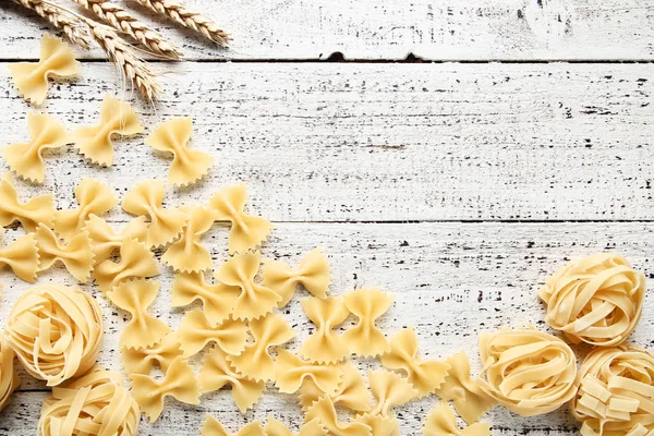 Different uncooked pasta on white wooden table