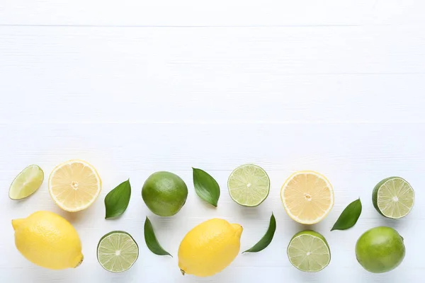 Lemons and limes with green leafs on white wooden table