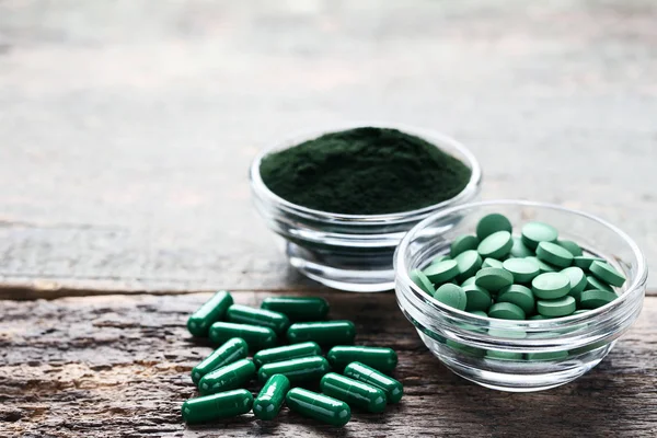 Spirulina powder and tablets in bowls on grey wooden table