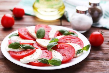 Mozzarella peyniri, domates ve fesleğen yaprakları üzerinde kahverengi ahşap masa