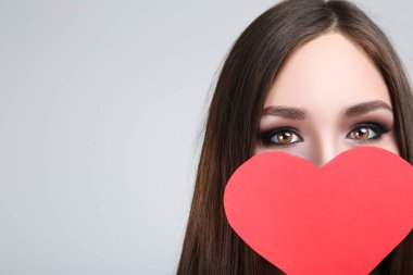 Gri arka plan üzerinde kırmızı kağıt kalp tutan güzel kadın