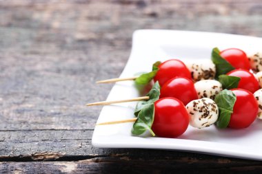 Mozzarella peyniri, domates ve fesleğen yaprakları gri ahşap masa üzerine sopalarla