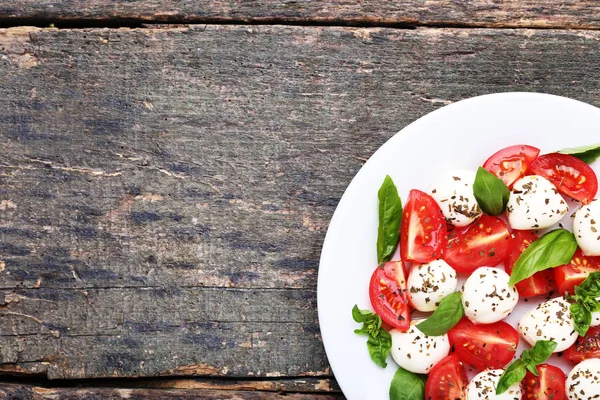 木桌上盘子里的莫扎雷拉 西红柿和罗勒叶 — 图库照片