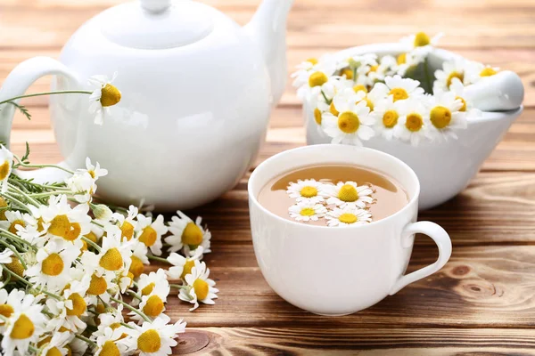 茶色の木製のテーブルにカモミールの花とお茶のカップ — ストック写真