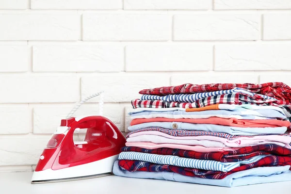 Stack of folded clothes with electric iron on brick wall background