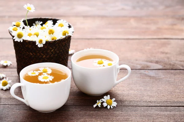 茶色の木製のテーブルにカモミールの花とお茶のカップ — ストック写真