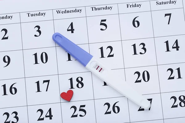 Pregnancy test on paper calendar with red heart