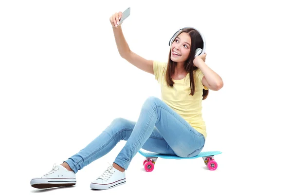 拿着耳机坐在滑板上自拍自拍的年轻女孩 — 图库照片