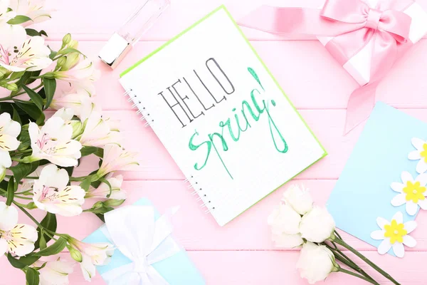 Fresh flowers, gift boxes and notepad with text Hello Spring on pink wooden table