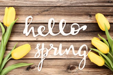 Ahşap masa üzerinde merhaba bahar metinle sarı laleler buket