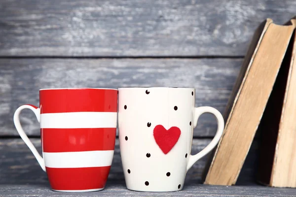 Cups with red heart and old books on grey wooden table