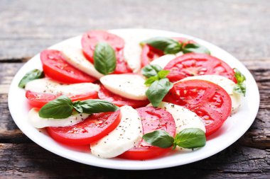 Mozzarella peyniri, domates ve fesleğen yaprakları üzerinde gri ahşap masa