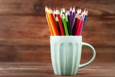 Kupası ahşap masa üzerinde renkli kalemler