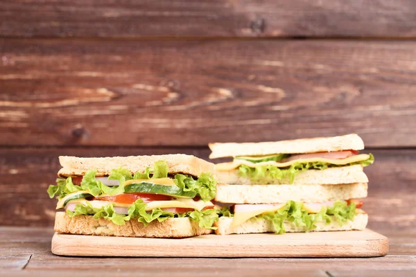 茶色の木製の背景にまな板とおいしいサンドイッチ — ストック写真