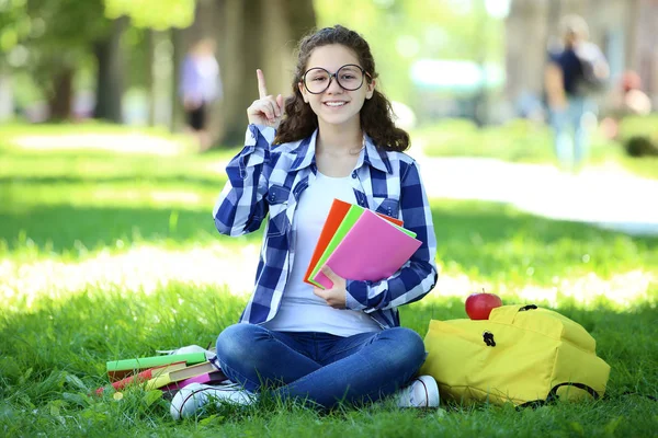 ノートブックとバックパックの公園で座っている若い女の子 — ストック写真