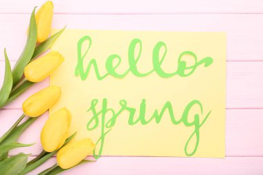 Ahşap masa üzerinde merhaba bahar metinle sarı laleler buket