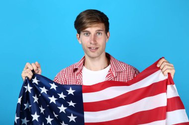 Bir Amerikan bayrağı mavi arka plan üzerinde tutan güzel genç adam