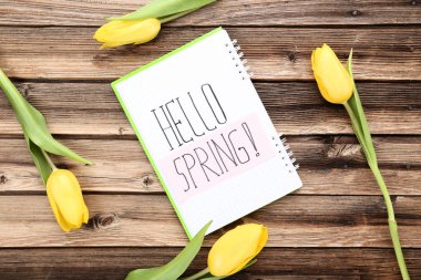 Ahşap masa üzerinde not defteri ve metin Merhaba yaylı Sarı laleler buket