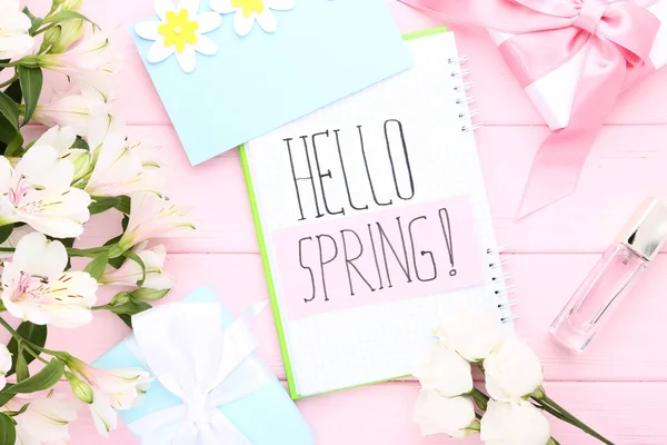 Fresh flowers, gift boxes and notepad with text Hello Spring on pink wooden table