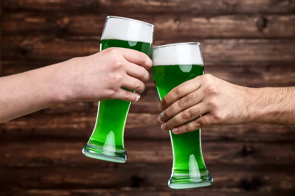 St. Patrick\'s Day. Glasses of green beer in male hands on wooden background