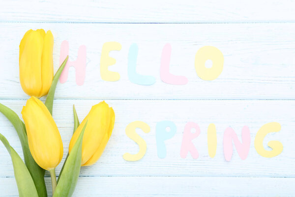Bouquet of yellow tulips with text Hello Spring on wooden table