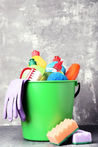 Bottles with detergent and cleaning tools on grey background