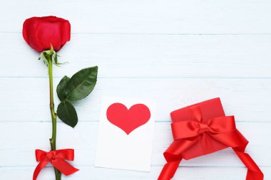 Ahşap masa üzerinde hediye kutusu ve greeitng kartı ile kırmızı gül