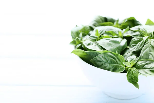 Grön basilika blad i skål på träbord — Stockfoto