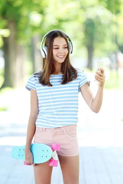 Νεαρό κορίτσι με πατίνι, ακουστικά και smartphone σε το par — Φωτογραφία Αρχείου