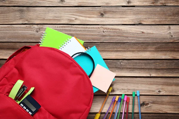 Roter Rucksack mit Schulmaterial auf braunem Holztisch — Stockfoto
