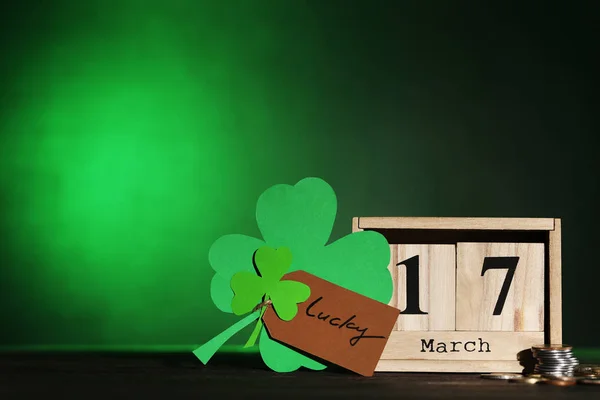 Hojas de trébol con calendario de madera y monedas sobre fondo verde — Foto de Stock