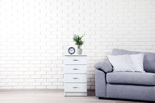 White bedside table near grey sofa with pillows on brick wall ba — Stock Photo, Image
