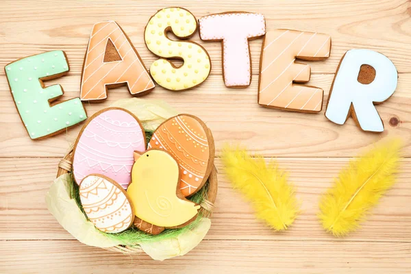 Galletas de jengibre con palabra Pascua y plumas amarillas sobre madera — Foto de Stock