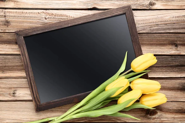 Boeket van gele tulpen met lege frame op bruin houten tafel — Stockfoto