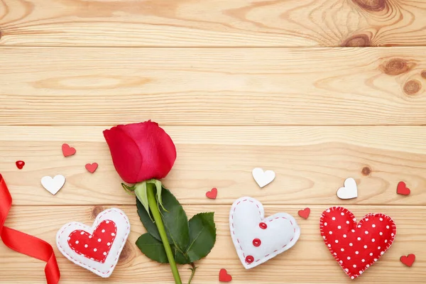 Red rose with fabric hearts and ribbon on brown wooden table — Stock Photo, Image