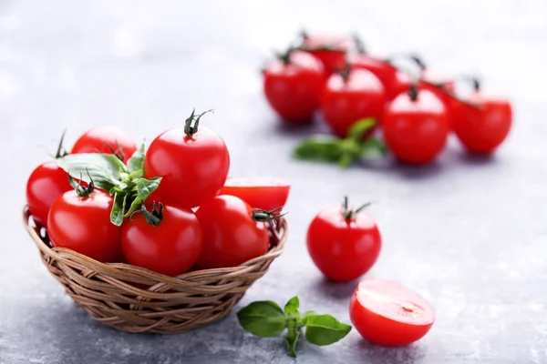 Kiraz domates fesleğen ile sepette yapraklar üzerinde gri ahşap masa — Stok fotoğraf