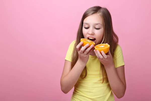 Niedliche junge Mädchen essen orangefarbene Früchte auf rosa Hintergrund — Stockfoto
