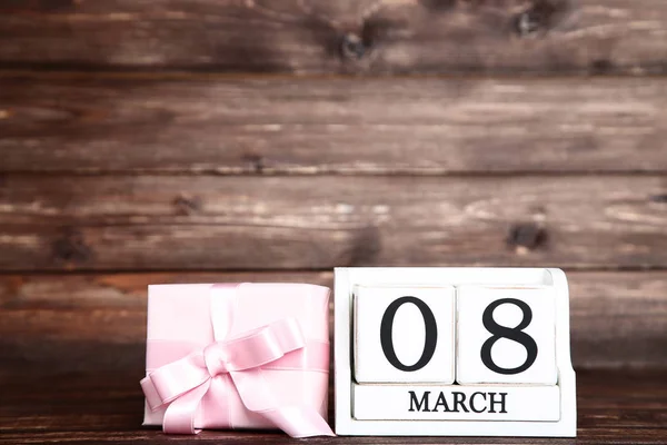 Frauentag auf Holzkalender mit Geschenkbox auf braunem Hintergrund — Stockfoto