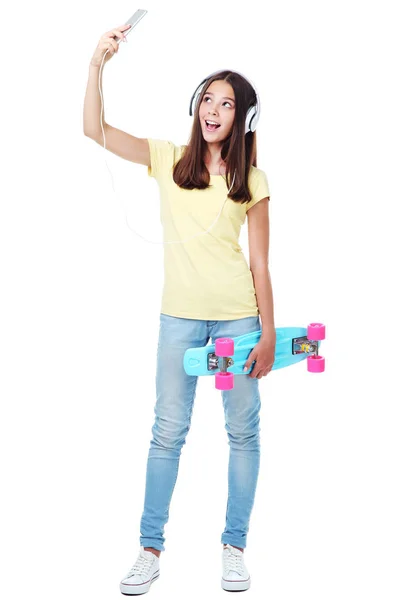 年轻的女孩与滑板和耳机制作自拍 — 图库照片