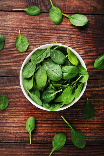 Spinach leafs in bowl on brown wooden table