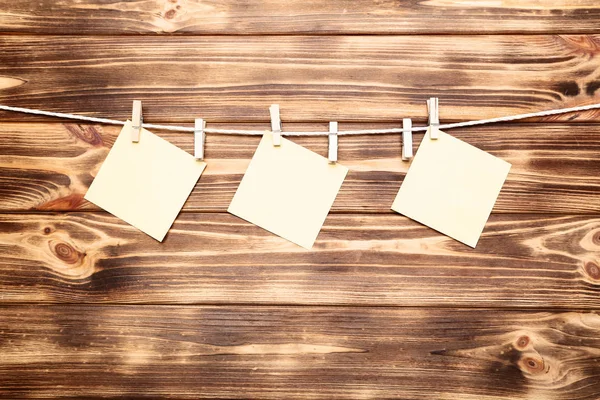 Pinzas de tela con hojas de papel en blanco colgadas en un fondo de madera — Foto de Stock